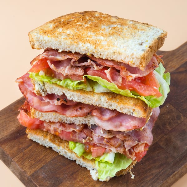 A towering triple-decker bacon, lettuce, and tomato sandwich on toasted bread, served on a wooden board.