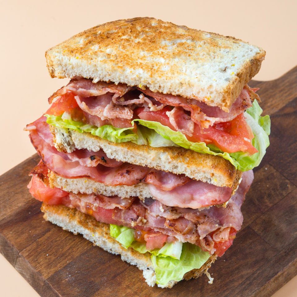 A towering triple-decker bacon, lettuce, and tomato sandwich on toasted bread, served on a wooden board.