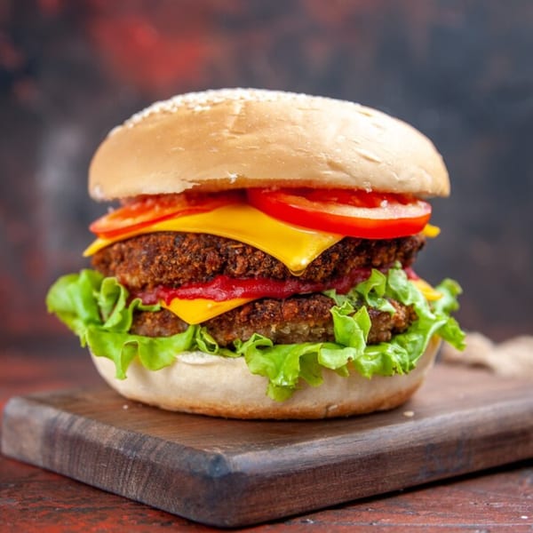 Double cheeseburger from Sharkies Bar & Grill with lettuce, tomato, and ketchup on a wooden board.