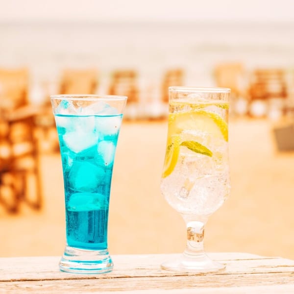 Two refreshing drinks, one blue and one clear with lemon and mint, on a wooden surface.